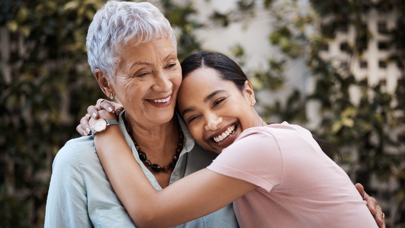 A senior mom is hugged by her adult daughter.